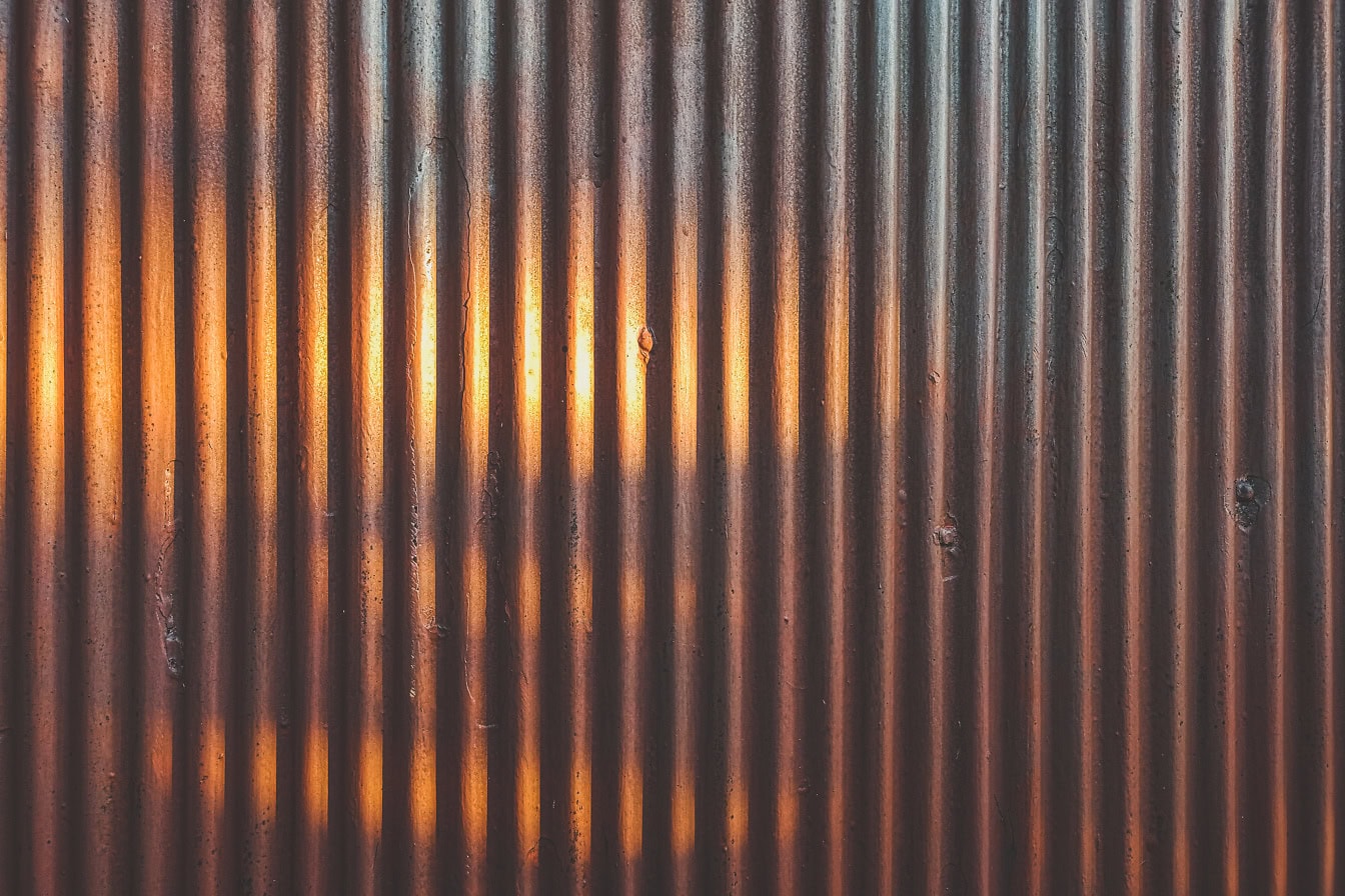 Текстура старого ржавого металлического листа с множеством вертикальных линий и тенью на красновато-коричневой краске, которая отслаивается от поверхности