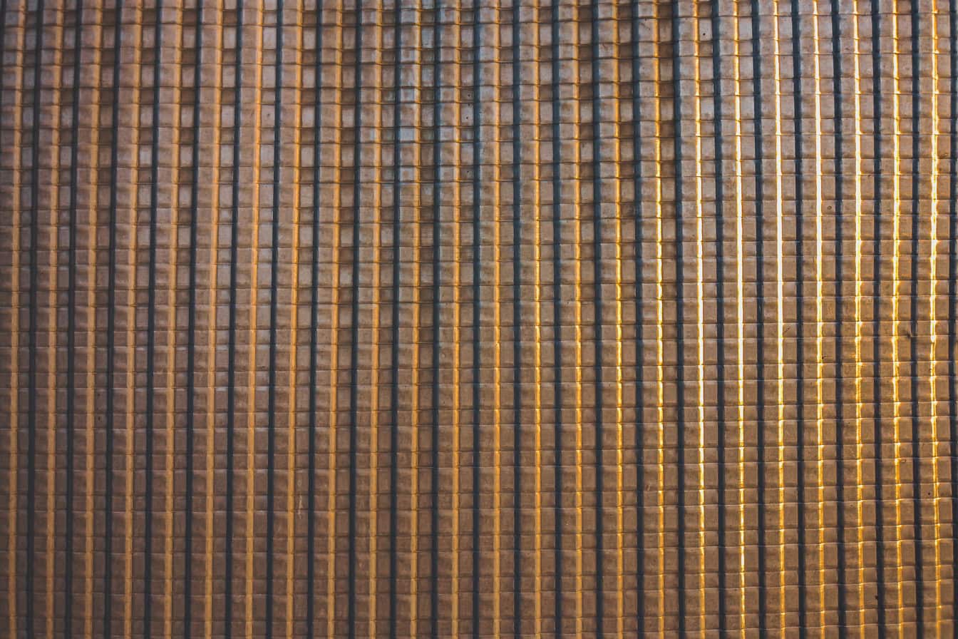 Textura de una lámina de metal de color marrón amarillento brillante con muchas líneas verticales y horizontales que forman un patrón geométrico con cuadrados
