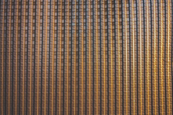 Texture di una lastra di metallo bruno-giallastra lucida con molte linee verticali e orizzontali che creano un motivo geometrico con quadrati