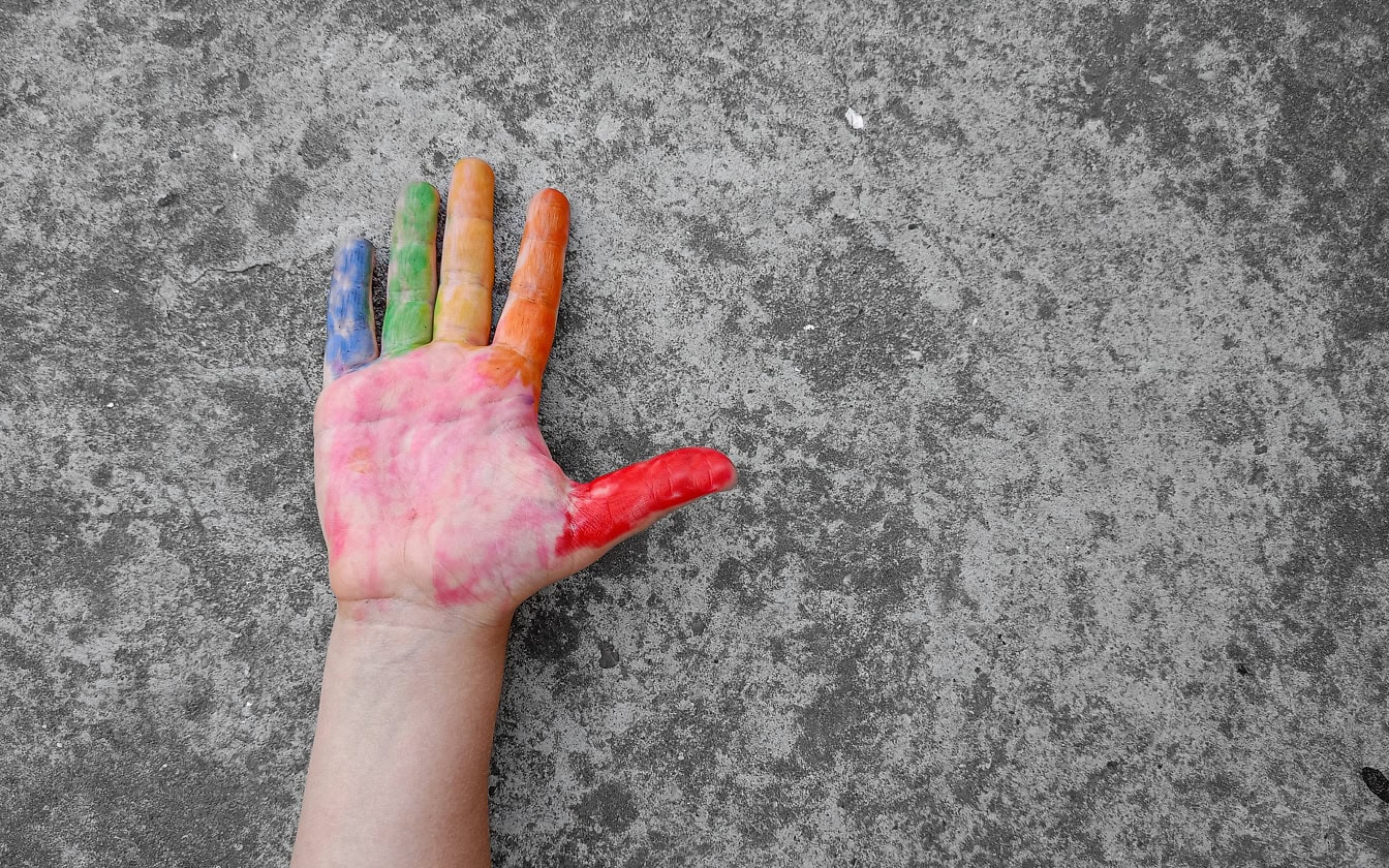 Käsi harmaalla betonilla värillisillä sormilla eri väreissä punaisesta ja oranssinkeltaisesta vihreään ja siniseen
