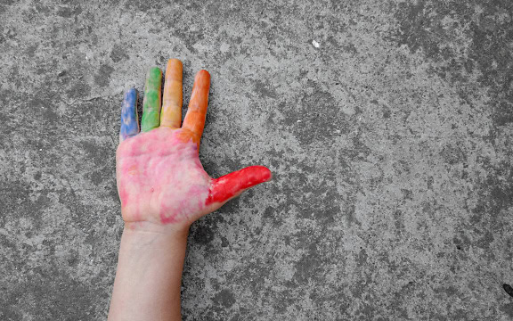 Mano su cemento grigio con dita colorate in diversi colori dal rosso e arancio-giallo al verde e blu