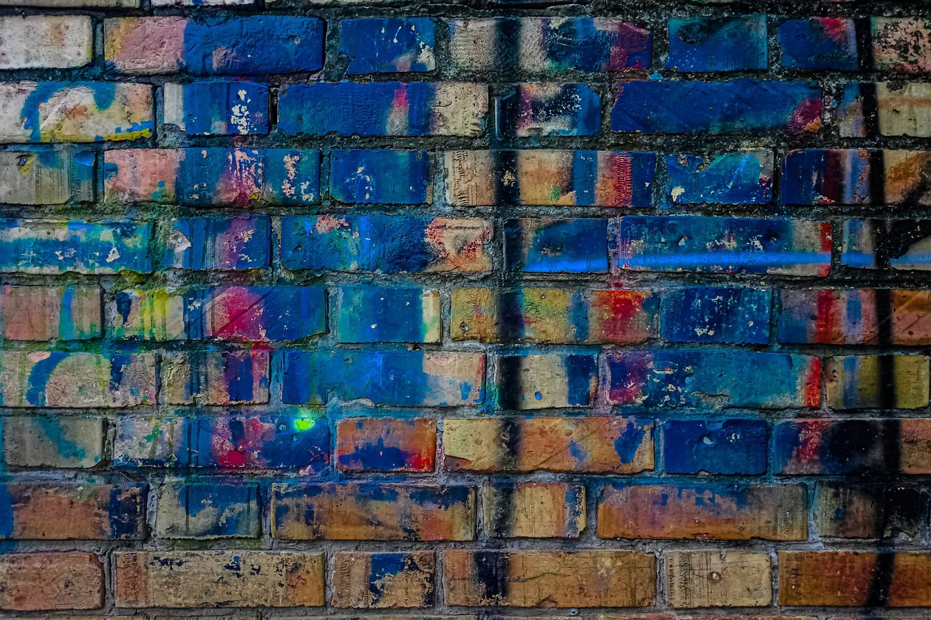 Texture of an old dirty brick wall with dark blue paint on it and with old graffiti