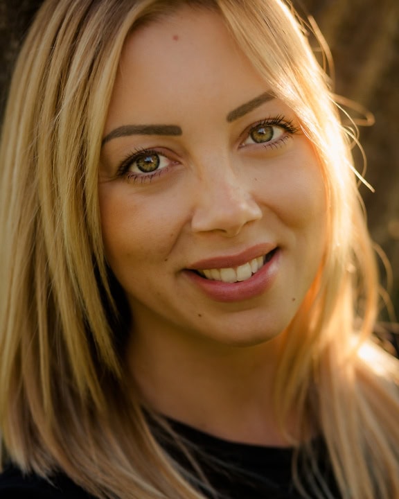 Um retrato em close-up de um rosto incrivelmente bonito de uma jovem com longos cabelos loiros sorrindo para a câmera