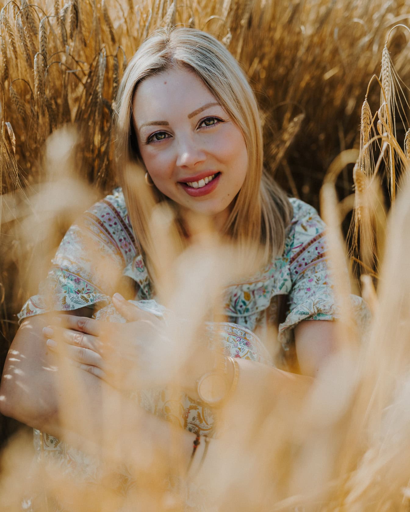 Una donna bionda di bellezza mozzafiato seduta e sorridente in un campo di grano