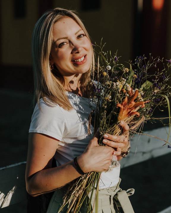 Portrait of a wonderfully beautiful young woman with long blonde hair holding a bouquet of wildflowers