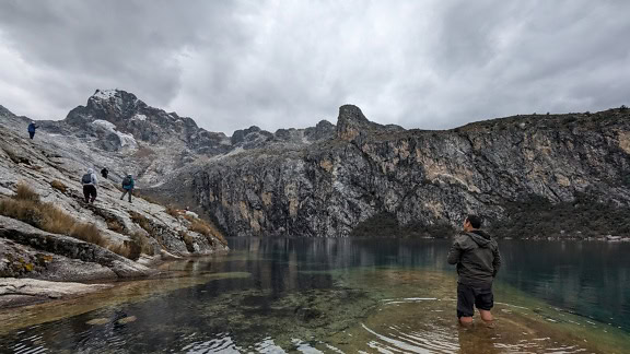 Мъж стои в студеното езеро Чаруп в природен парк в Перу с планини на заден план