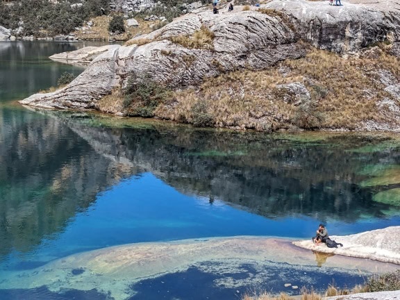 Persona sentada en una roca en la costa de un lago Charup en Parque Natural en Perú