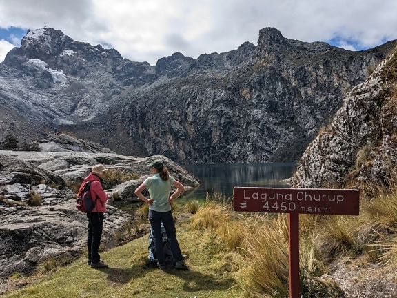Női túrázók egy tábla mellett állnak a Churup tónál, a nemzeti parkban, Huaraz város közelében, Áncash régióban, Peruban, Latin-Amerikában