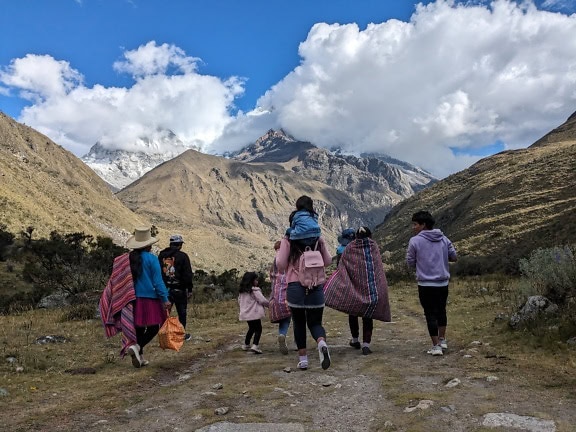 O familie peruviană făcând drumeții împreună pe o potecă din fața munților din parcul natural din Peru
