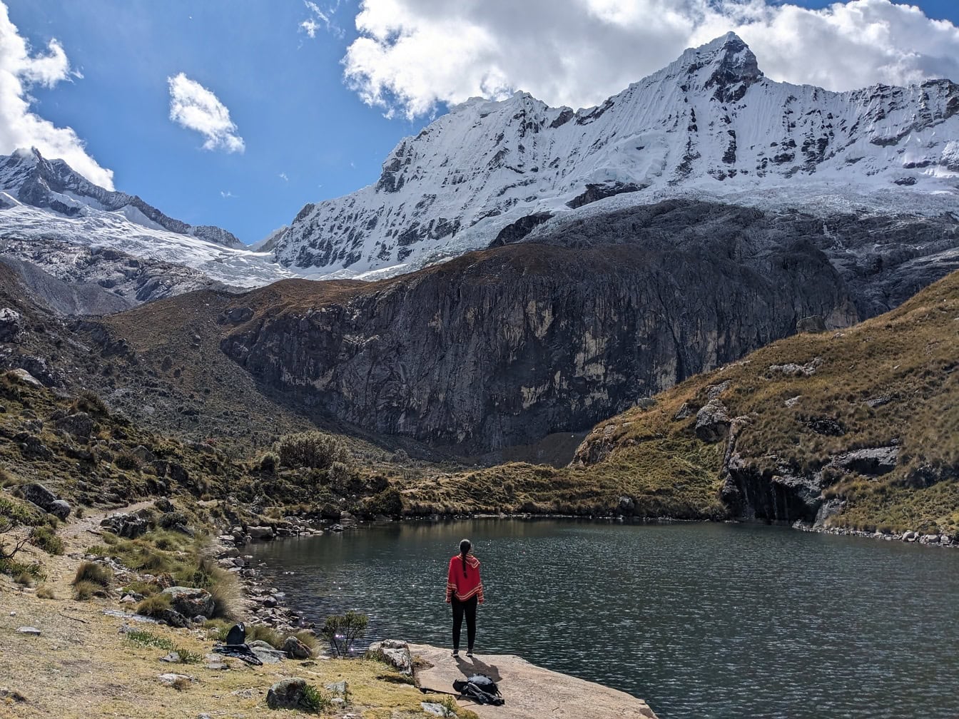Persoană în poncho tradițional peruvian stă pe malul unui lac din lanțul muntos Cordillera Blanca din Anzi din Peru, America Latină