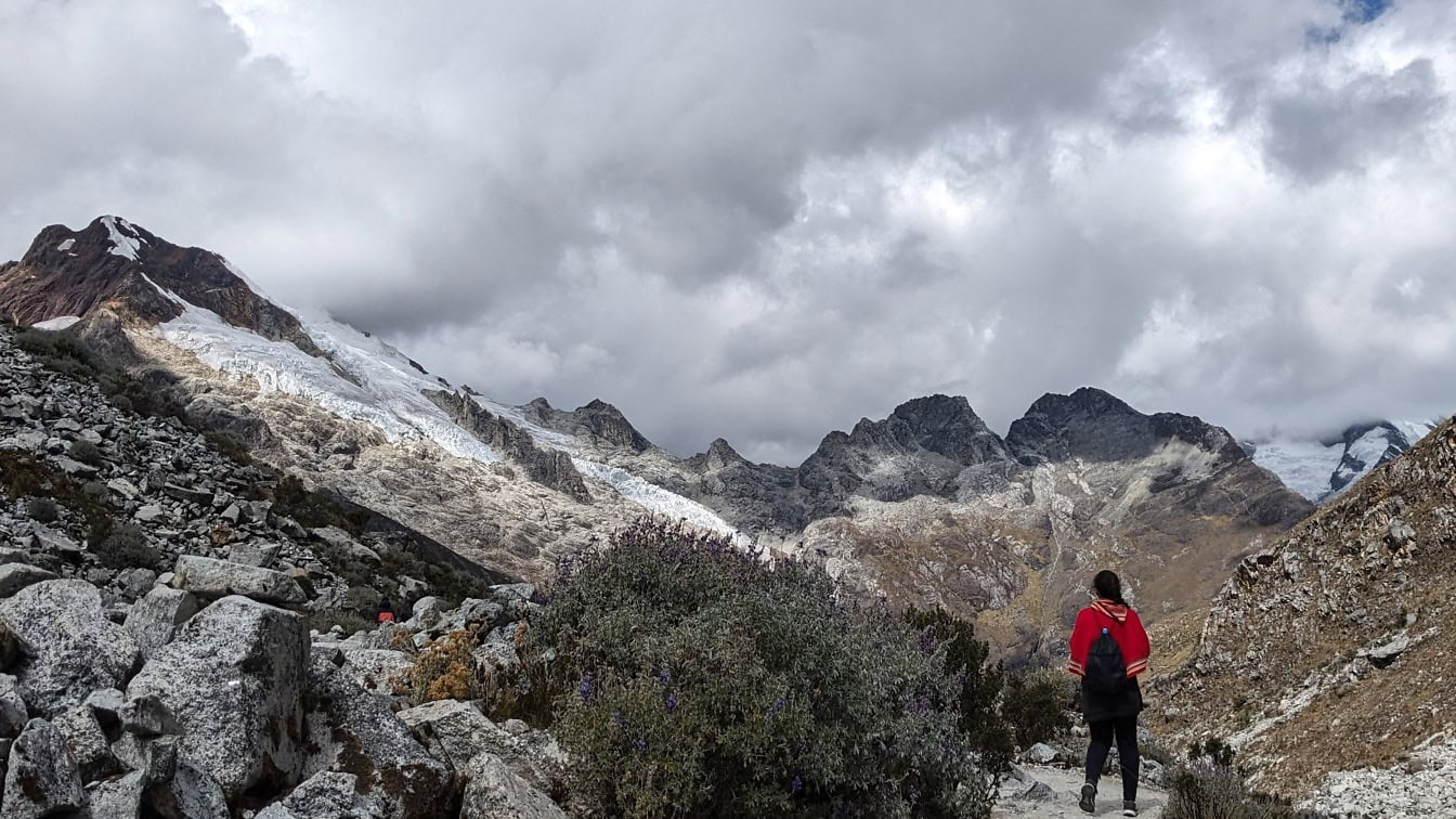 전통적인 짙은 빨간색 페루 판초를 입은 등산가가 바위 산에 서 있습니다