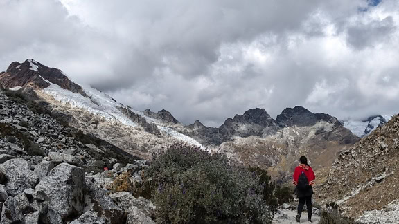 Un alpinist într-un poncho peruvian tradițional roșu închis stă pe un munte stâncos