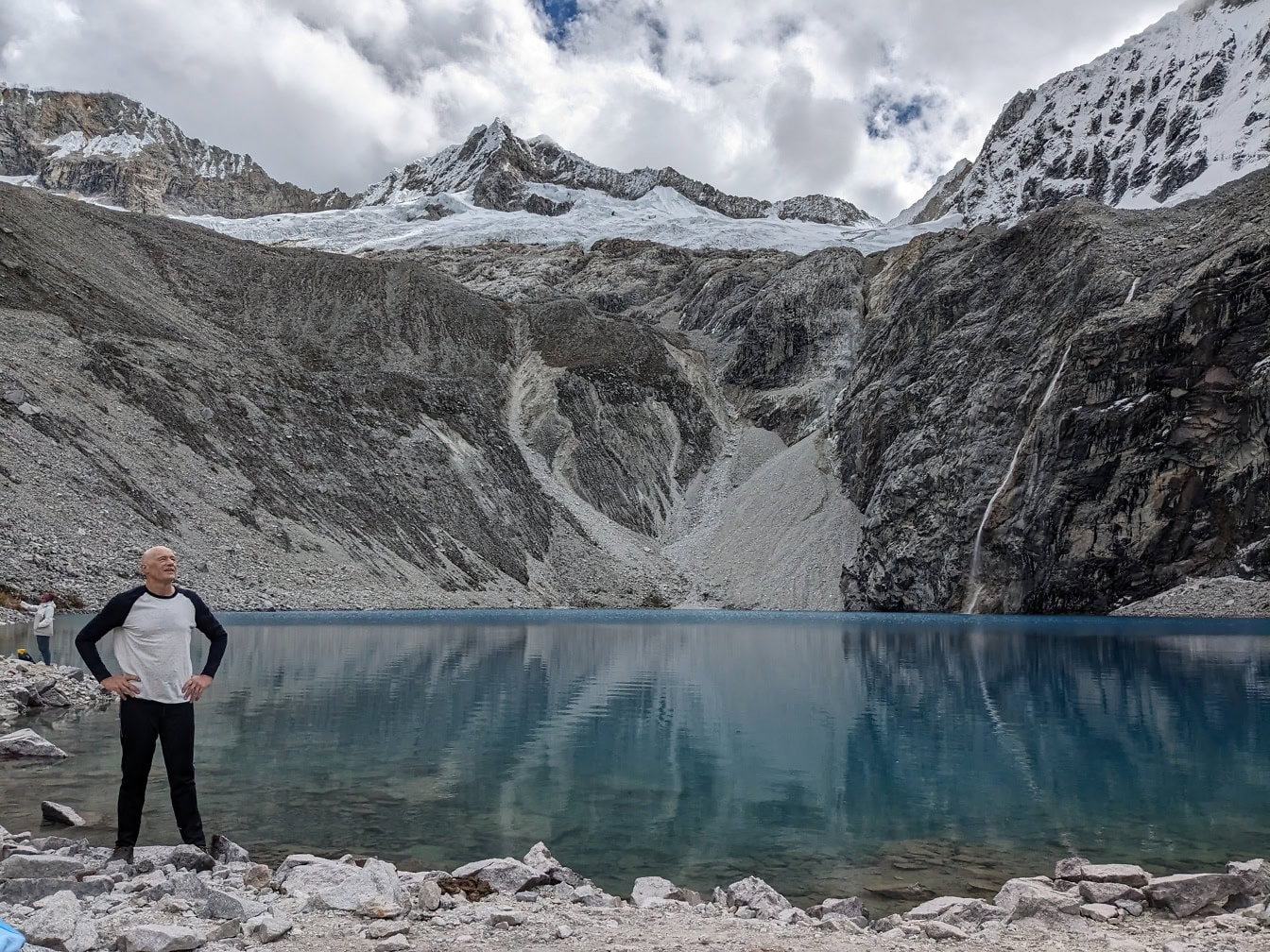 Man standing on a rocky shore of the Lake 69 or Laguna 69 in Huascaran national park near the Huaraz in Peru, landscape of a Latin America