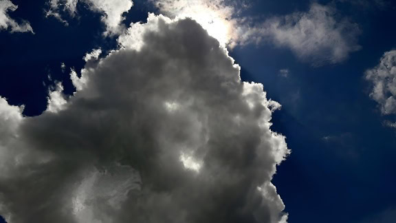 Tummansininen taivas ja aurinko pilvien takana