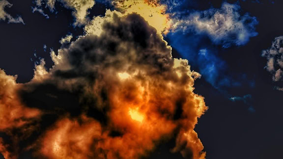 Πολύ σκούρο μπλε ουρανό με τον ήλιο πίσω από τα πορτοκαλί-κίτρινα σύννεφα