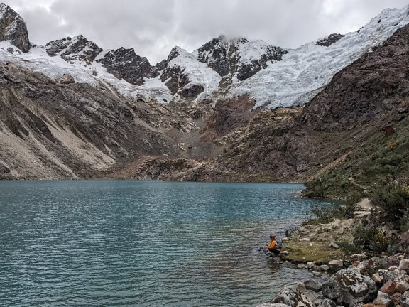 Landskap av en sjö Congelada de Rocotuyoc i regionen Ancash i Peru med en person som sitter på en kust