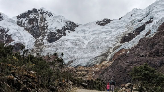 Man en kind lopen op een pad voor een gletsjer in Peru