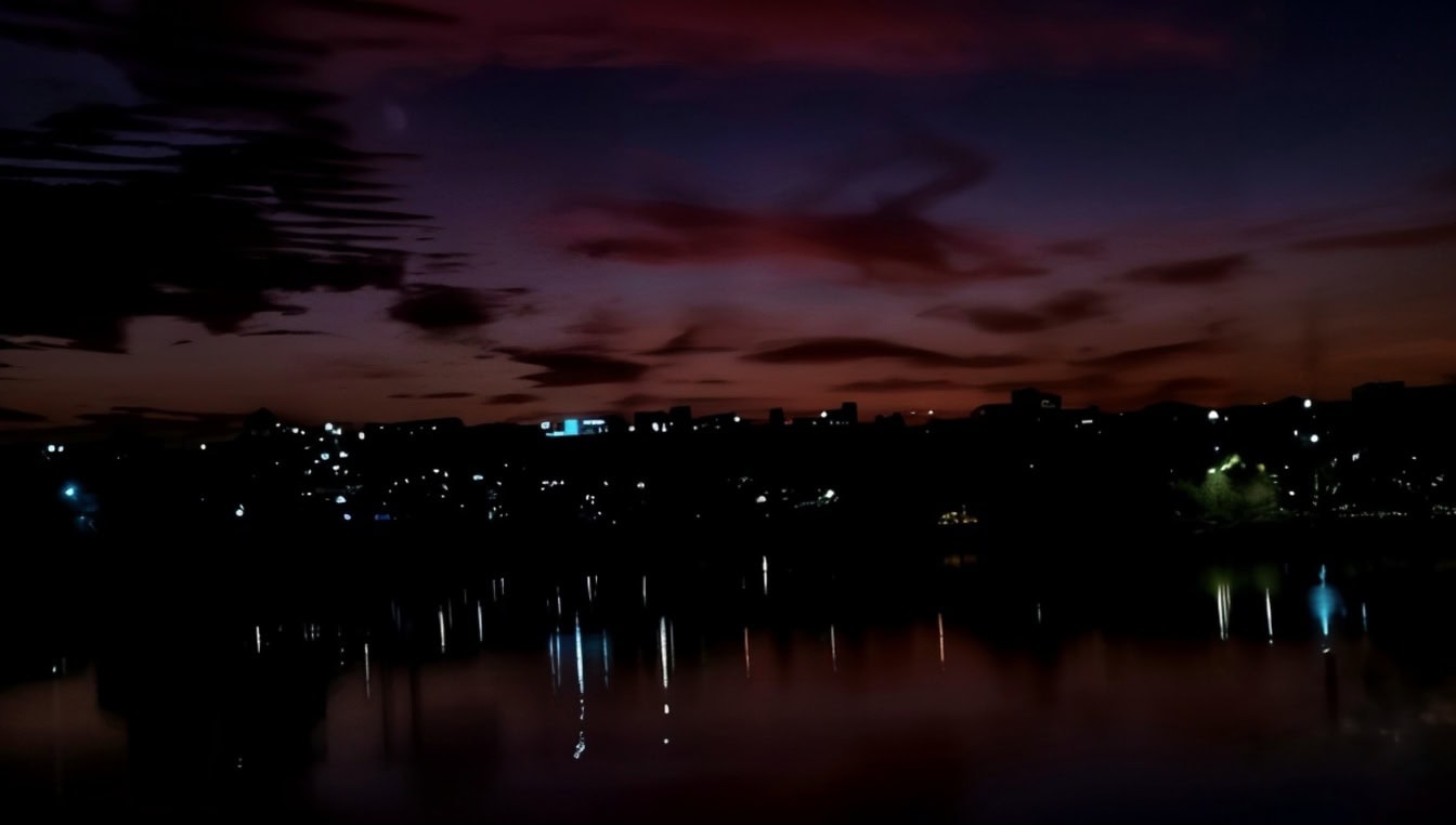 Orizontul orașului pe timp de noapte, cu o reflectare a luminilor orașului pe o apă calmă, cu cer roșu purpuriu închis ca fundal