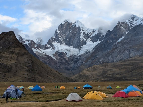 Grupa namiotów w dolinie z ośnieżonymi szczytami górskimi w tle