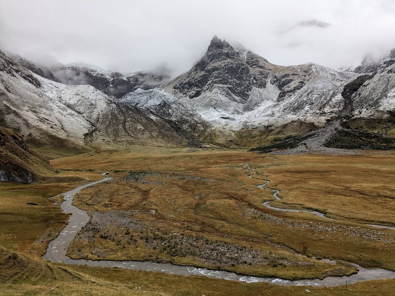 Rivier die door een vallei met met sneeuw behandelde bergen in het Cordillera Huayhuash-gebergte in Peru loopt