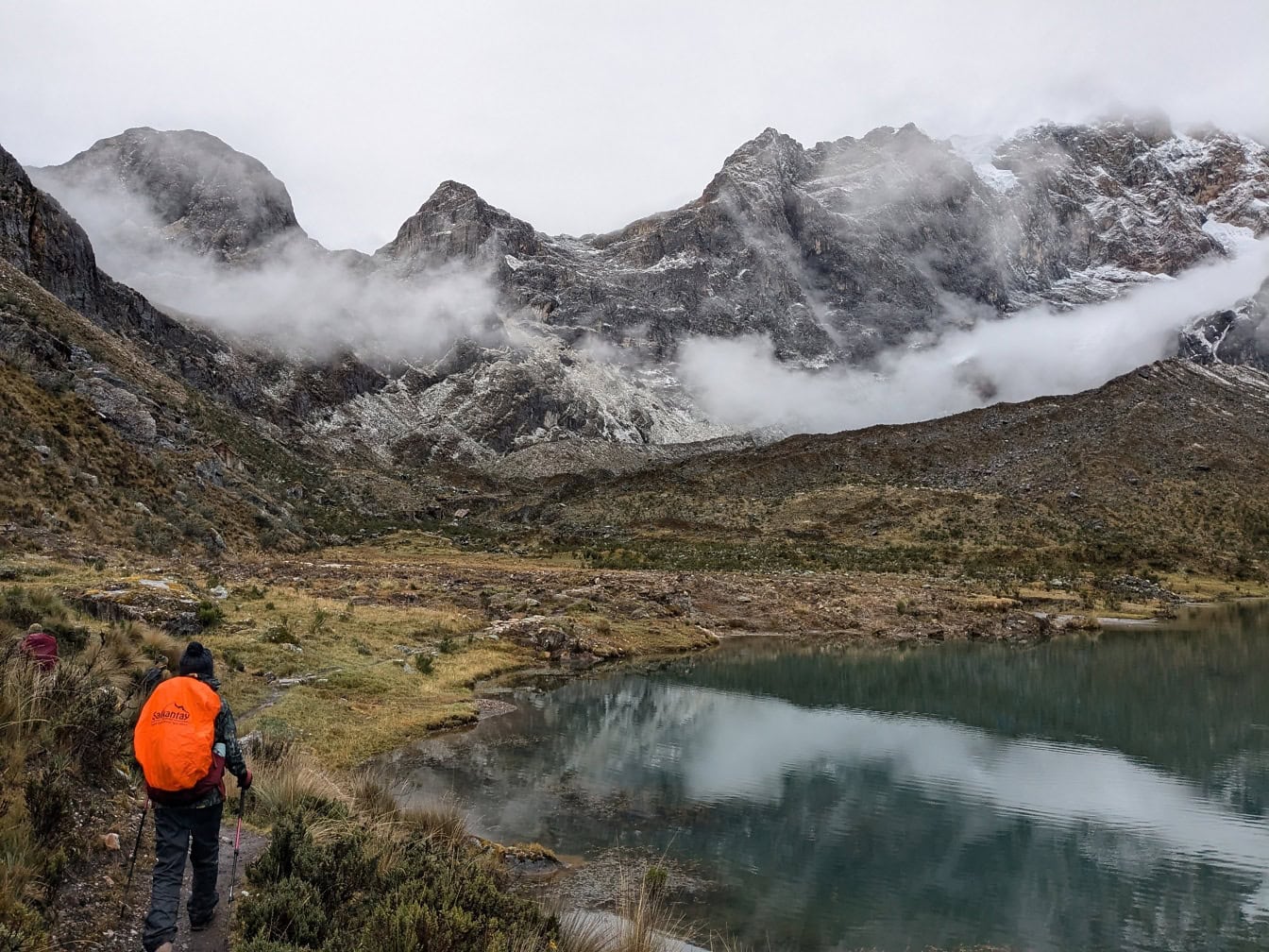 Persoană care merge pe o cărare lângă un lac din munți, la pasul Paso de Carhuac din lanțul muntos Cordillera Huayhuash din Peru