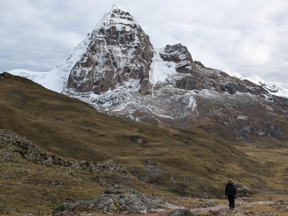 Mand går på en sti med en snedækket bjergtop i baggrunden