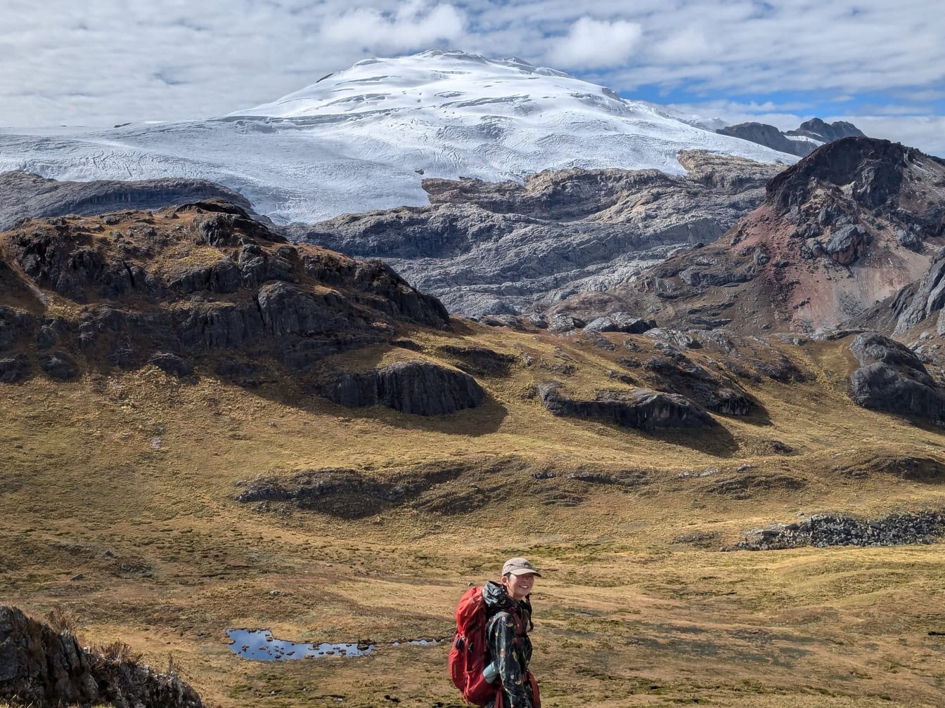 Pria Peru yang tersenyum mendaki di lapangan dengan gunung bersalju di latar belakang di Andes Peru