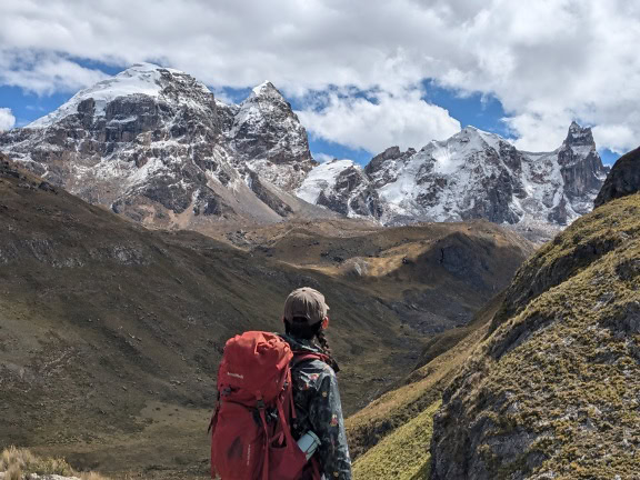 Excursionist cu rucsacul în spate privind o vale cu vârfuri montane înzăpezite la lanțul muntos Cordillera Huayhuash din Peru