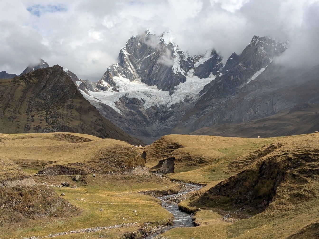 Râu de munte care trece printr-o vale din lanțul muntos Cordillera Huayhuash din Anzi din Peru, cu munți în fundal