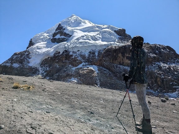 Henkilö seisoo vuorella, jonka taustalla näkyy lumen peittämä vuori Perun Andeilla