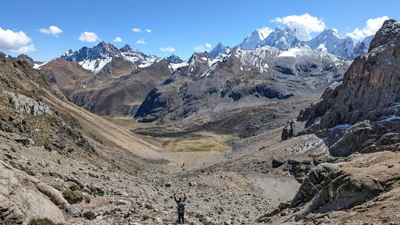 Person som står i en dal i forgrunnen ved fjellkjeden Cordillera Huayhuash i Andesfjellene i Peru med fjell i bakgrunnen