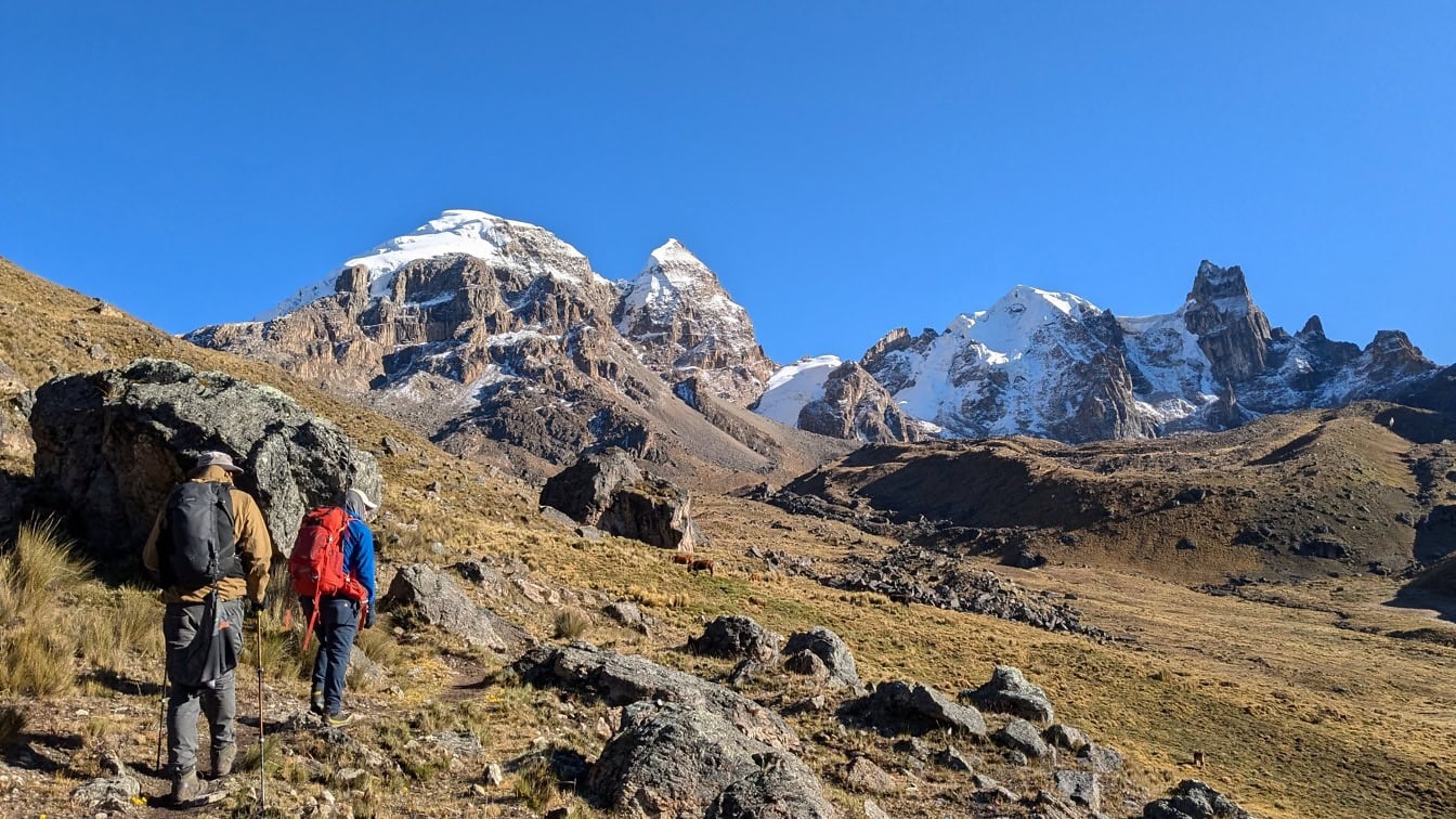 Kaksi moutain-kiipeilijää kävelemässä polulla, jonka taustalla on lumen peittämiä vuoria Perussa;
