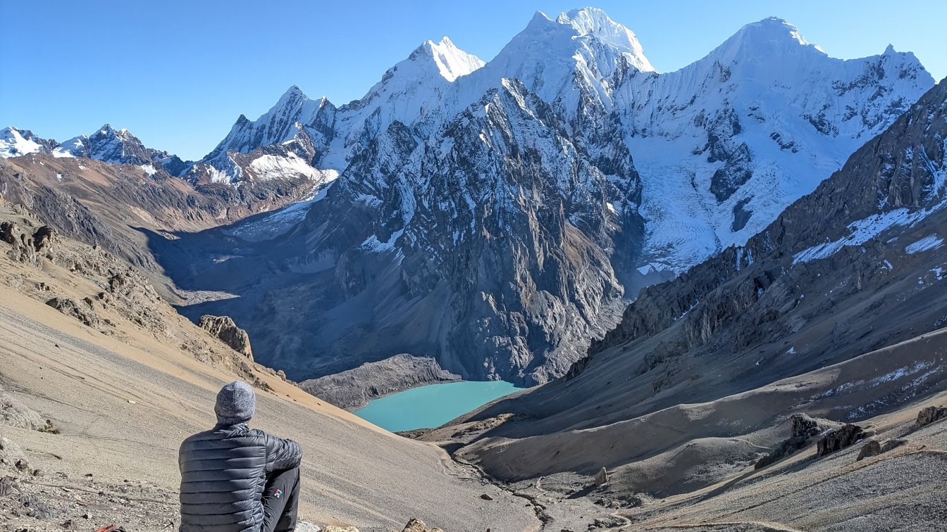 Planinar sjedi na planini i gleda jezero Palcacocha na planinskom lancu Cordillera Huayhuash u Andama Perua u Južnoj Americi
