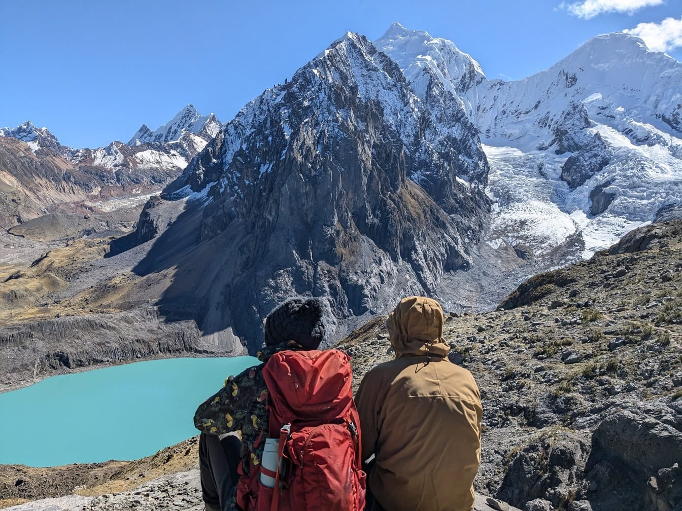 Dva lidé sedí a dívají se na jezero Palcacocha v údolí se zasněženými vrcholky hor v pohoří Cordillera Huayhuash v Peru