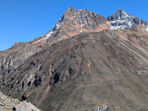 Osoba sedící na skále v pohoří Cordillera Huayhuash v peruánských Andách v pozadí