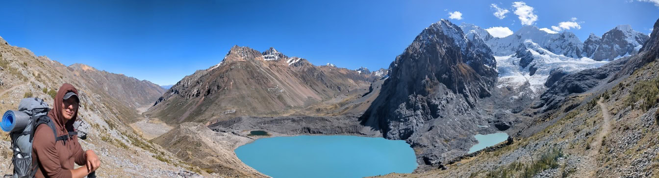 Panoramatický pohled na turistu s batohem na zádech v popředí a jezero v pohoří Cordillera Huayhuash v peruánských Andách v pozadí