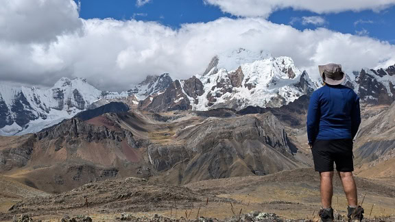 Мъж, стоящ пред планина в планинската верига Cordillera Huayhuash в Перу и наслаждаващ се на живописна гледка