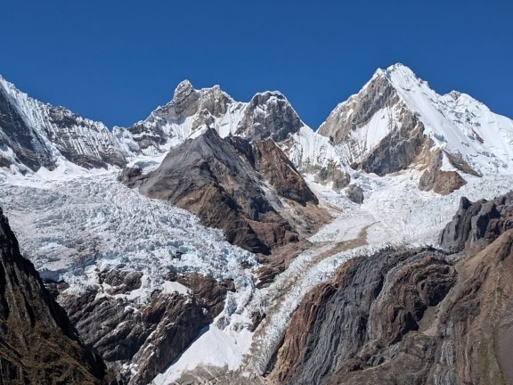 Frozen glacier at mountain peaks of a Cordillera Huayhuash mountain range in the Andes of Peru with a blue sky as background