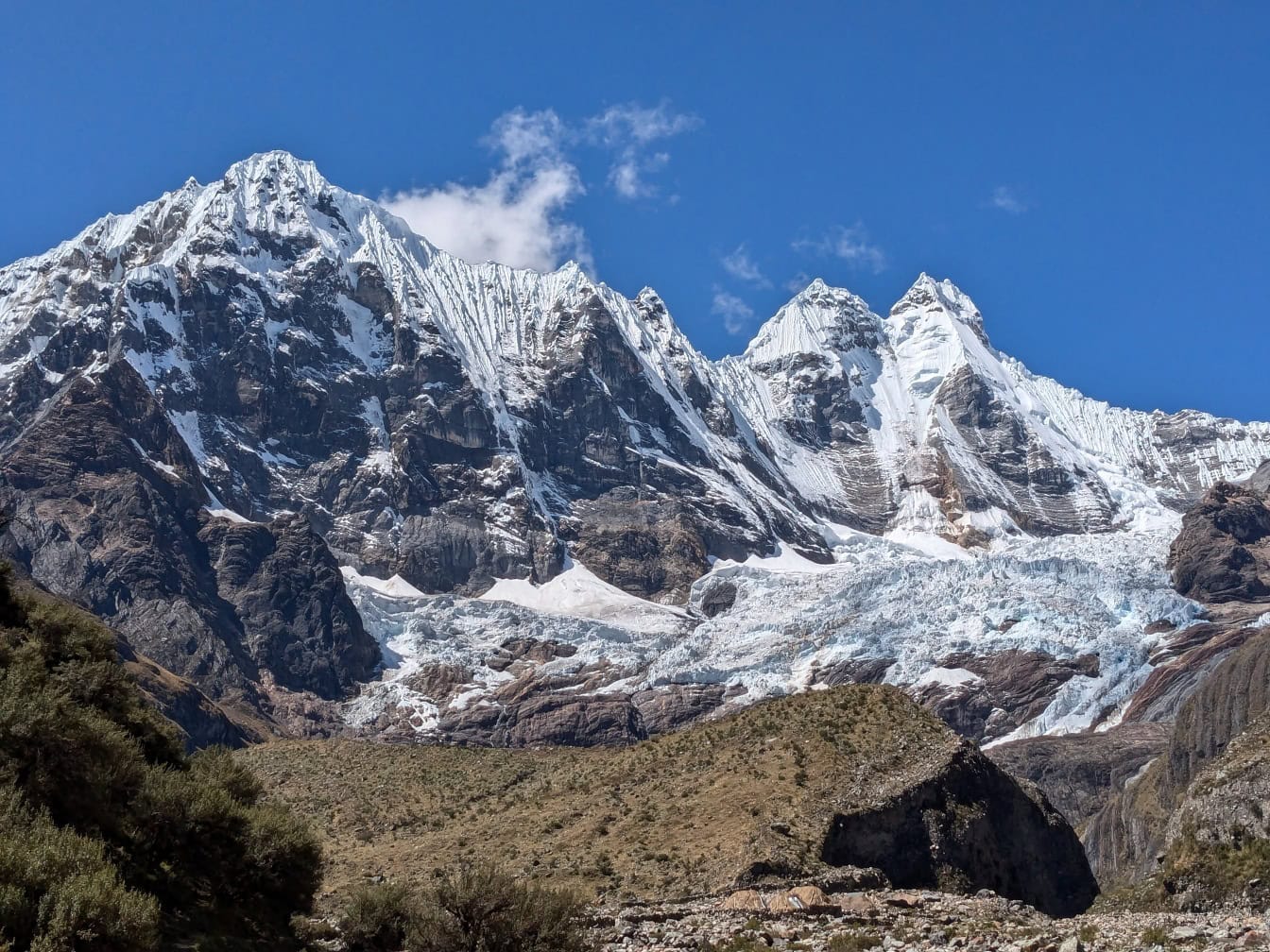 Snedækkede bjergtoppe ved Cordillera Huayhuash, en bjergkæde i Andesbjergene i Peru med en blå himmel i baggrunden