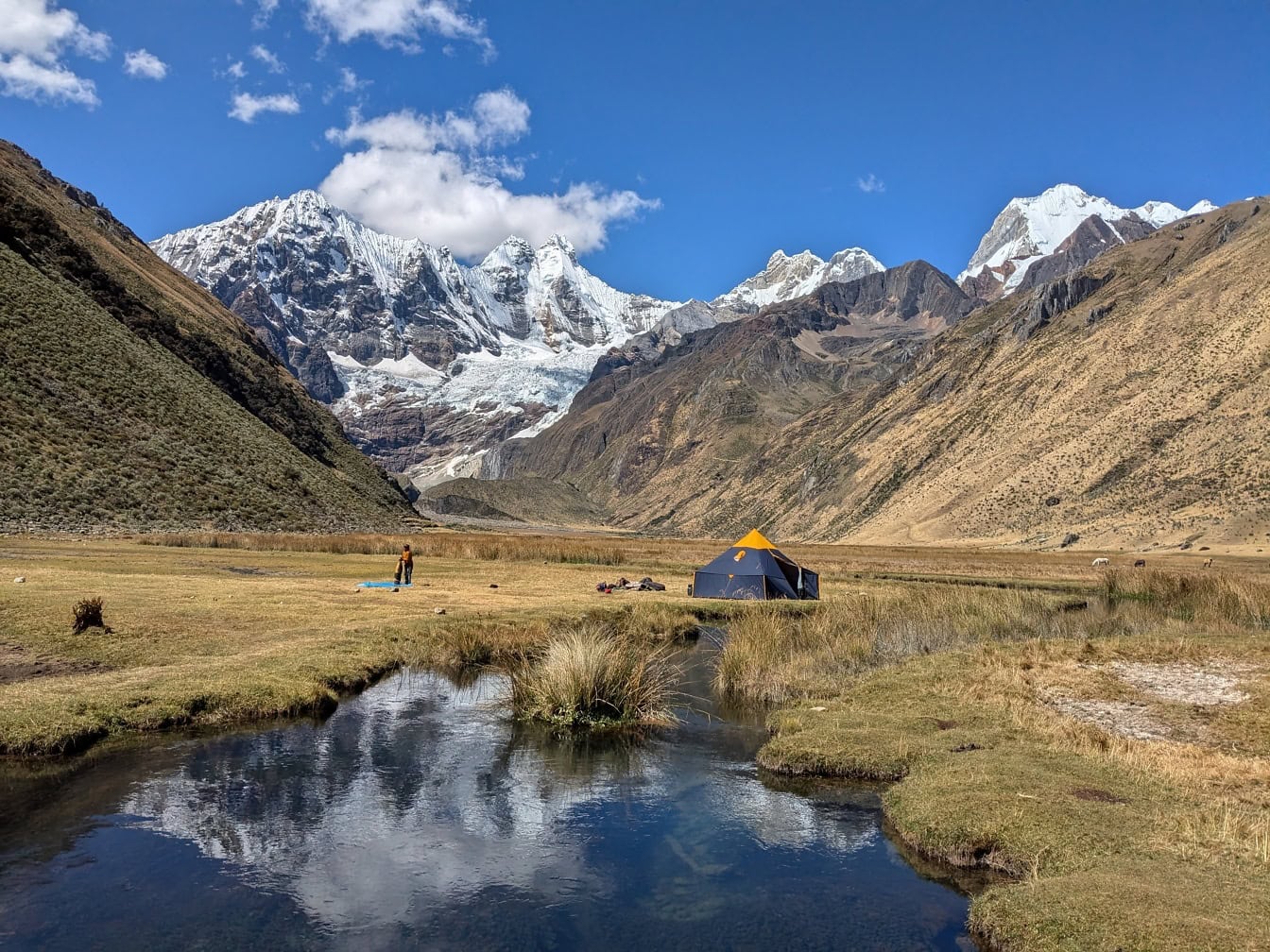 Tienda de campaña en la orilla de un río en un valle con la Cordillera Huayhuash, una cadena montañosa en los Andes en Perú