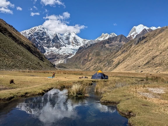 Tenda em uma margem de rio em um vale com Cordillera Huayhuash, uma cordilheira nos Andes no Peru