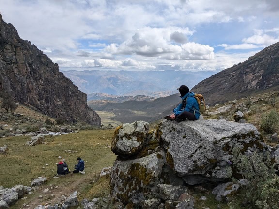 Backpack πεζοπόρος κάθεται σε ένα βράχο και απολαμβάνει πανόραμα της κοιλάδας και των βουνών στο φυσικό πάρκο του Περού