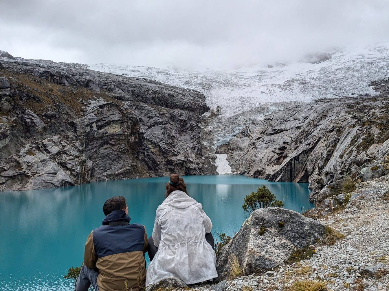 Mann und Frau sitzen am Ufer des Sees 513, einem Gletschersee am Fuße des Berges Nevado Hualcan im Huascaran-Nationalpark, Peru