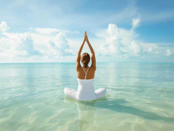 Mujer con ropa blanca pura sentada en el agua en posición de yoga con las manos levantadas en el aire