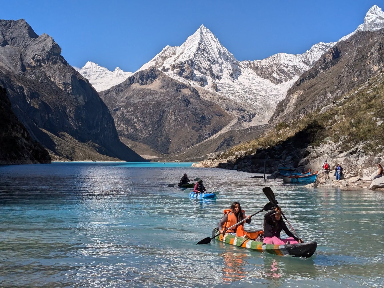 人们在秘鲁安第斯山脉科迪勒拉布兰卡的帕龙湖上划皮划艇，背景是山峰