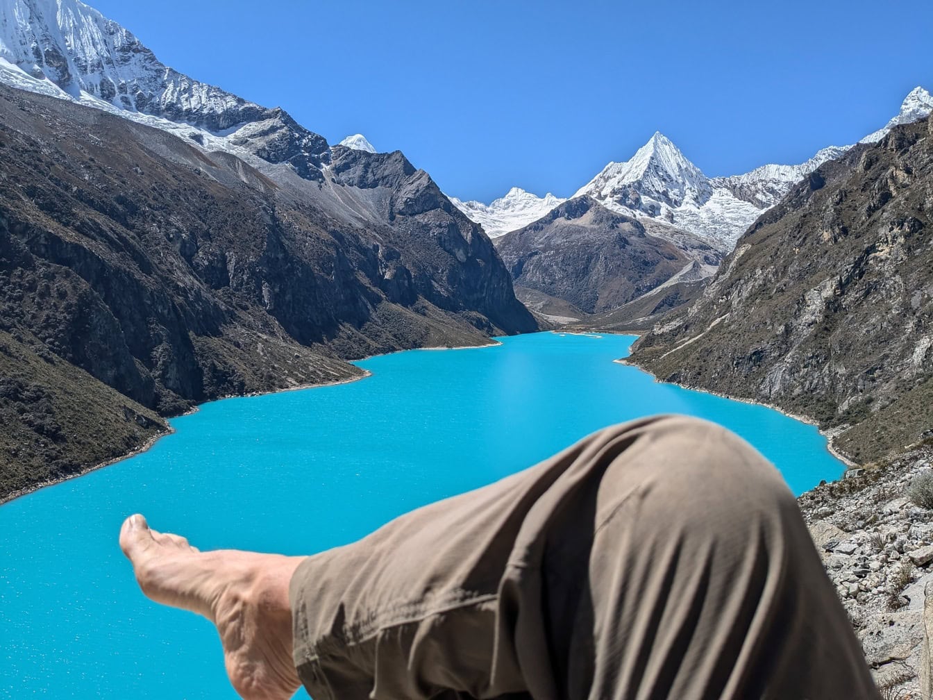 Kaki bertelanjang kaki seseorang di latar depan dengan danau Paron di latar belakang di Cordillera Blanca di Andes Peru