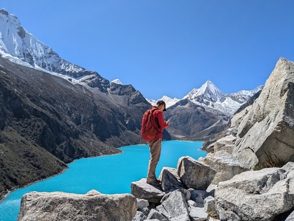 Mens die zich op rotsen bevinden die het Paron-meer bij Cordillera Blanca in de Andes van Peru bekijken