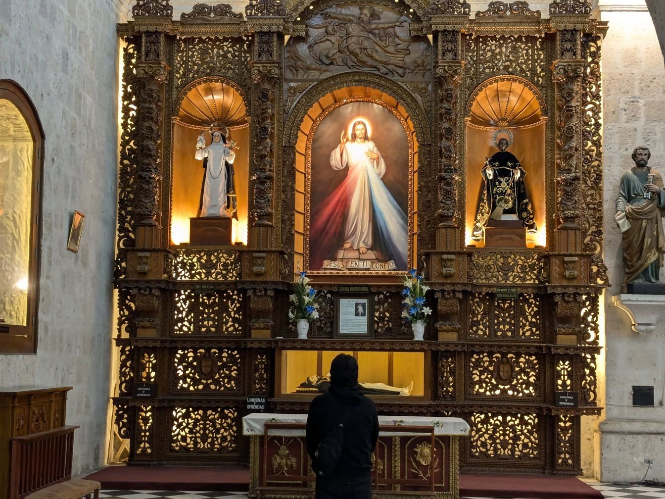 Henkilö, joka seisoo ja rukoilee koristeellisen alttarin edessä, jossa on Jeesuksen Kristuksen ikoni katolisessa kirkossa