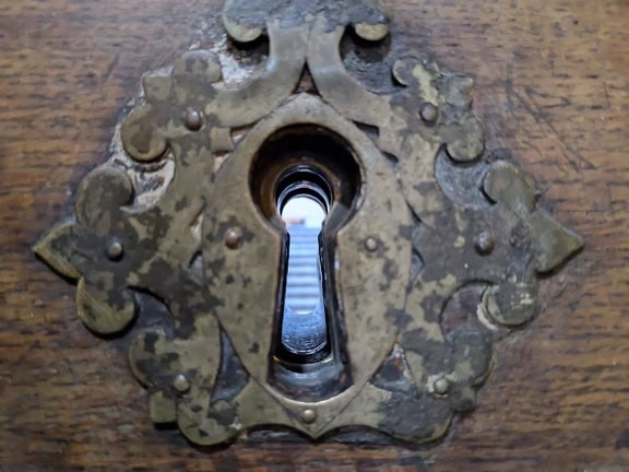 A view through an old ornate keyhole on a wooden front door