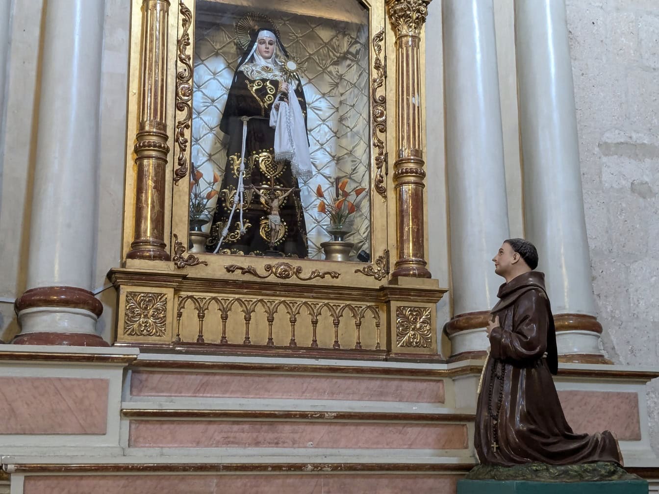 Standbeeld van een gebedsmens op zijn knieën voor standbeeld van non in een katholieke kerk in Peru